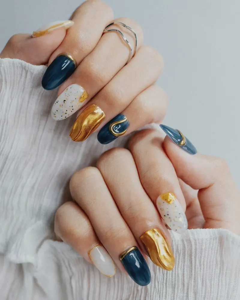Almond nails in navy, gold foil and speckled white, close up on both hands.