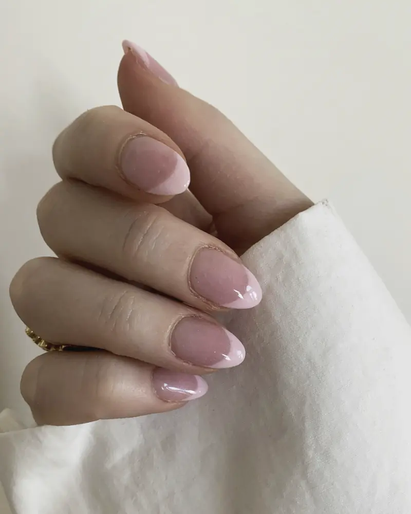 Almond nails in a milky pink, hand resting on a white cloth.