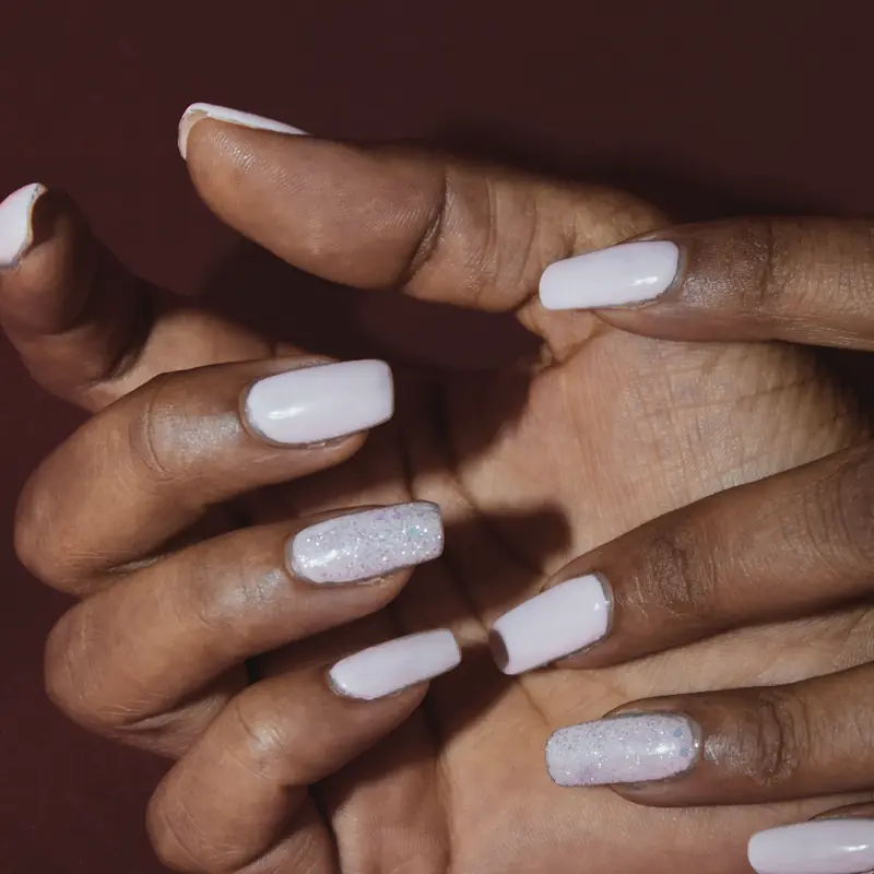 Long square nails in a soft lilac white, two with fine glitter, on a deep red background.
