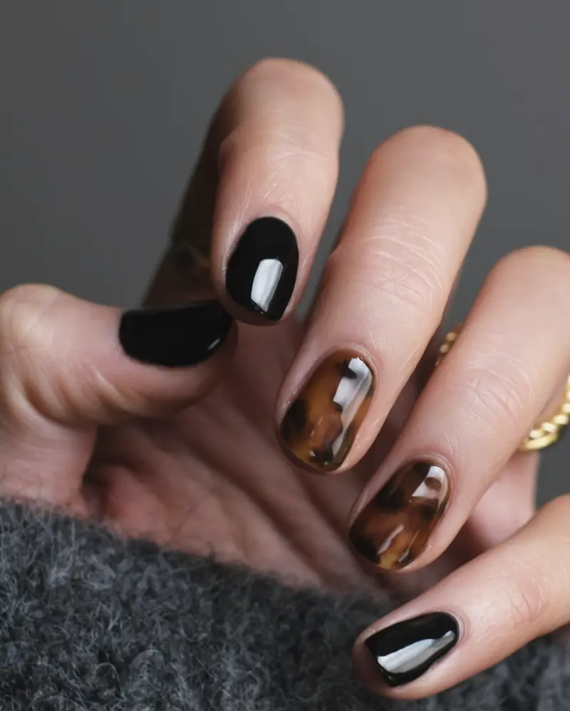 Short black gel nails with two tortoiseshell accent nails, close up, a grey knit cuff at the bottom edge.