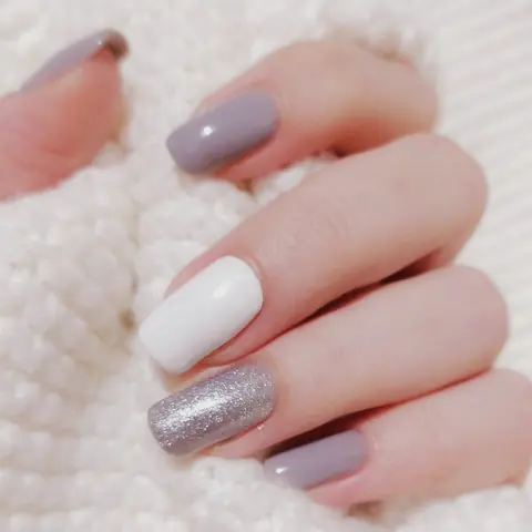 Square mauve nails with one white and one silver glitter accent, close up.