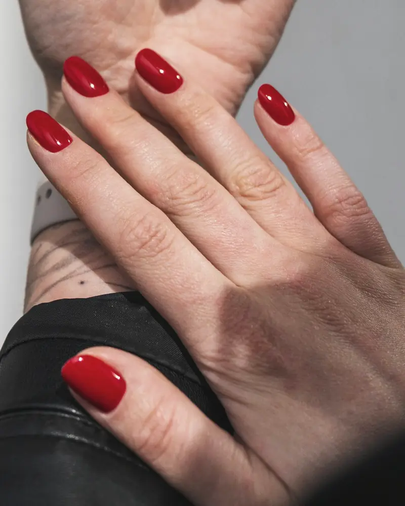 Short oval nails in a deep cherry red, one hand resting over the other wrist.